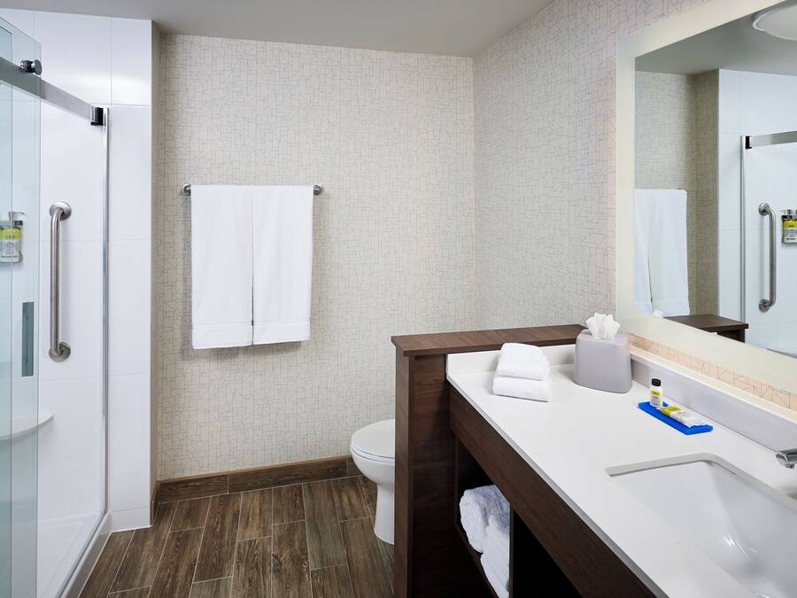 Un bagno moderno con box doccia in vetro, un WC bianco, un mobile lavabo in legno con specchio e un lavandino bianco.