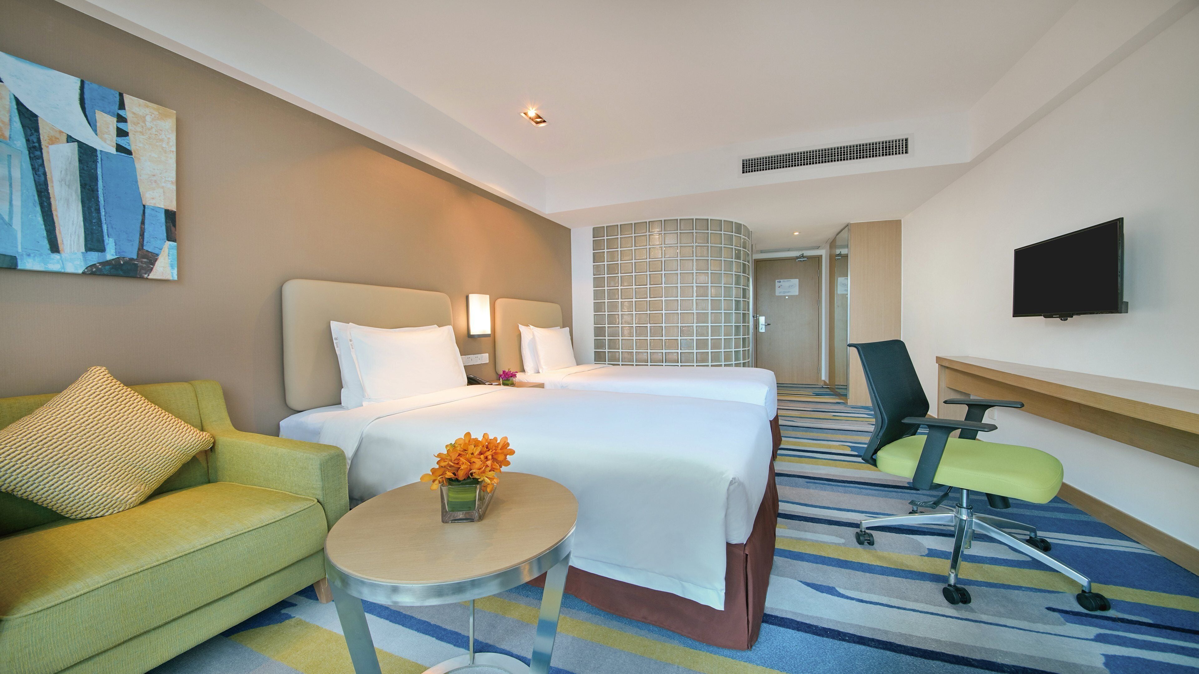 A hotel room with a bed, a desk, a chair, a television, and a painting on the wall.