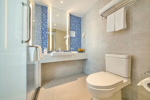 Une salle de bain moderne avec des toilettes blanches, un lavabo surmonté d’un miroir et une douche à parois de verre.