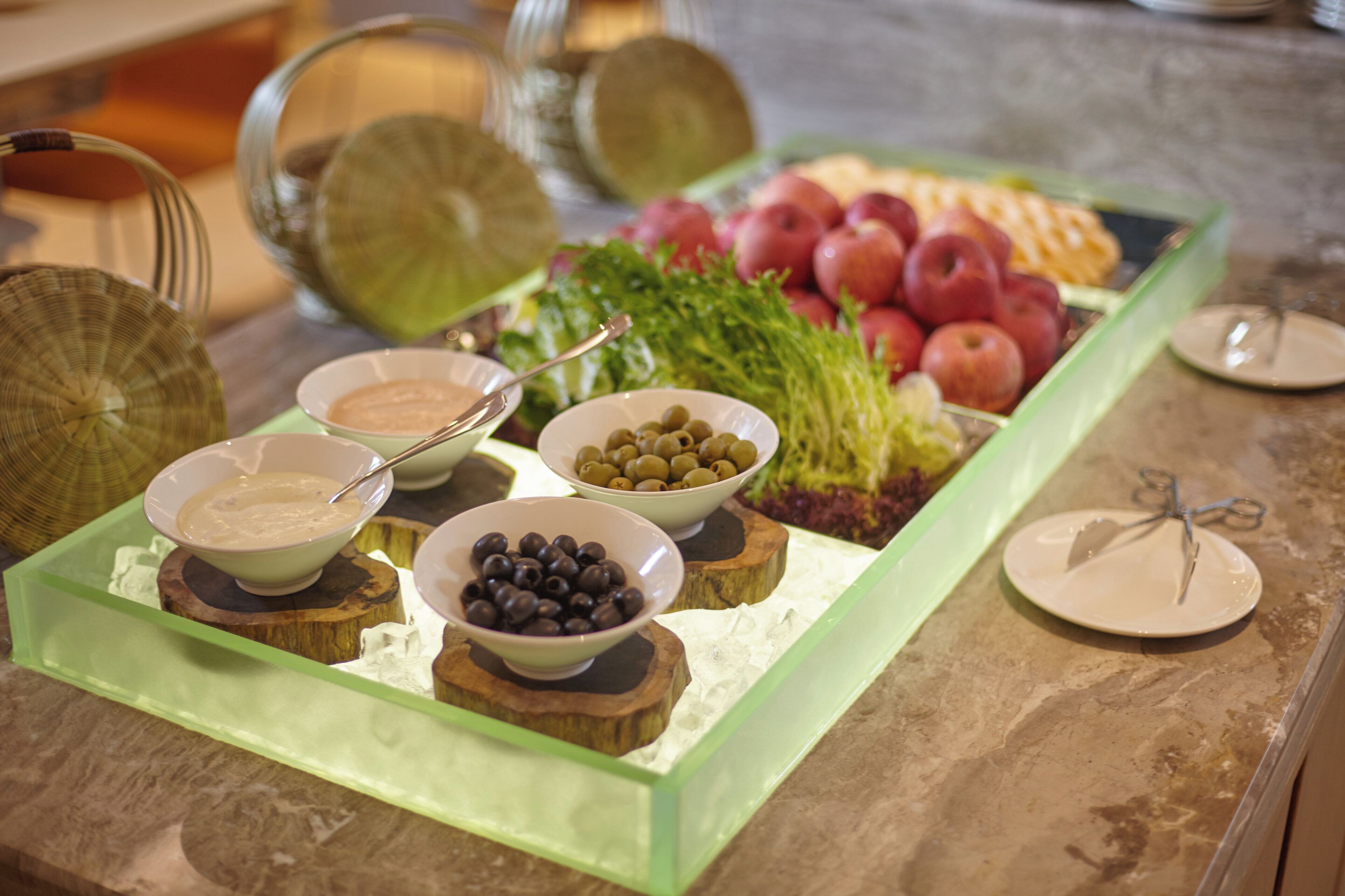 Una mesa de buffet con diversos alimentos, incluyendo aceitunas, manzanas y un tazón de sopa.