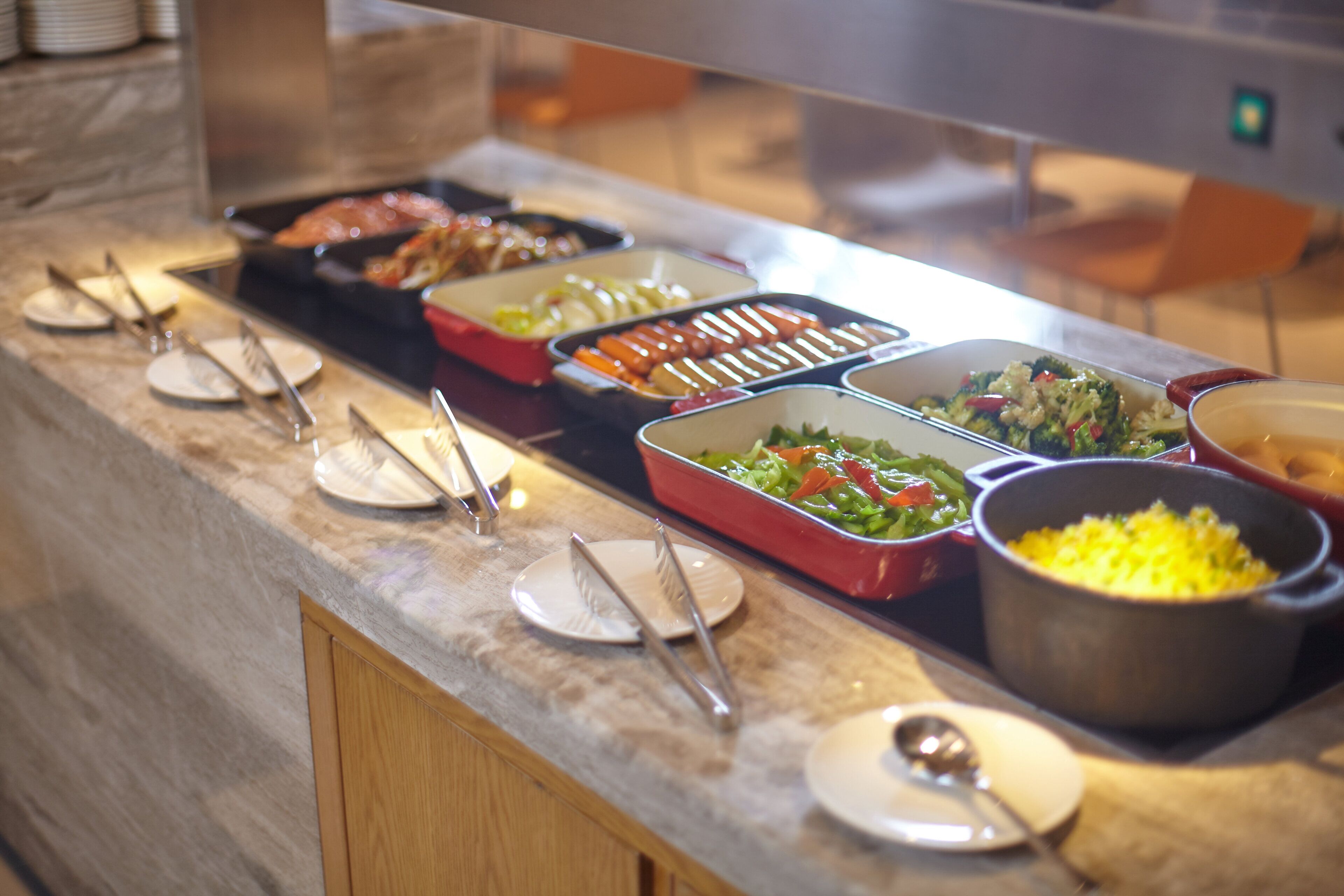 Un buffet proposant divers plats présentés dans des plateaux et des bols, avec des couverts disposés sur des assiettes et un comptoir en marbre.