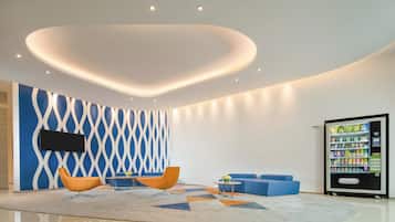 A modern lobby with a flat-screen TV, seating area, vending machine, and a decorative ceiling.