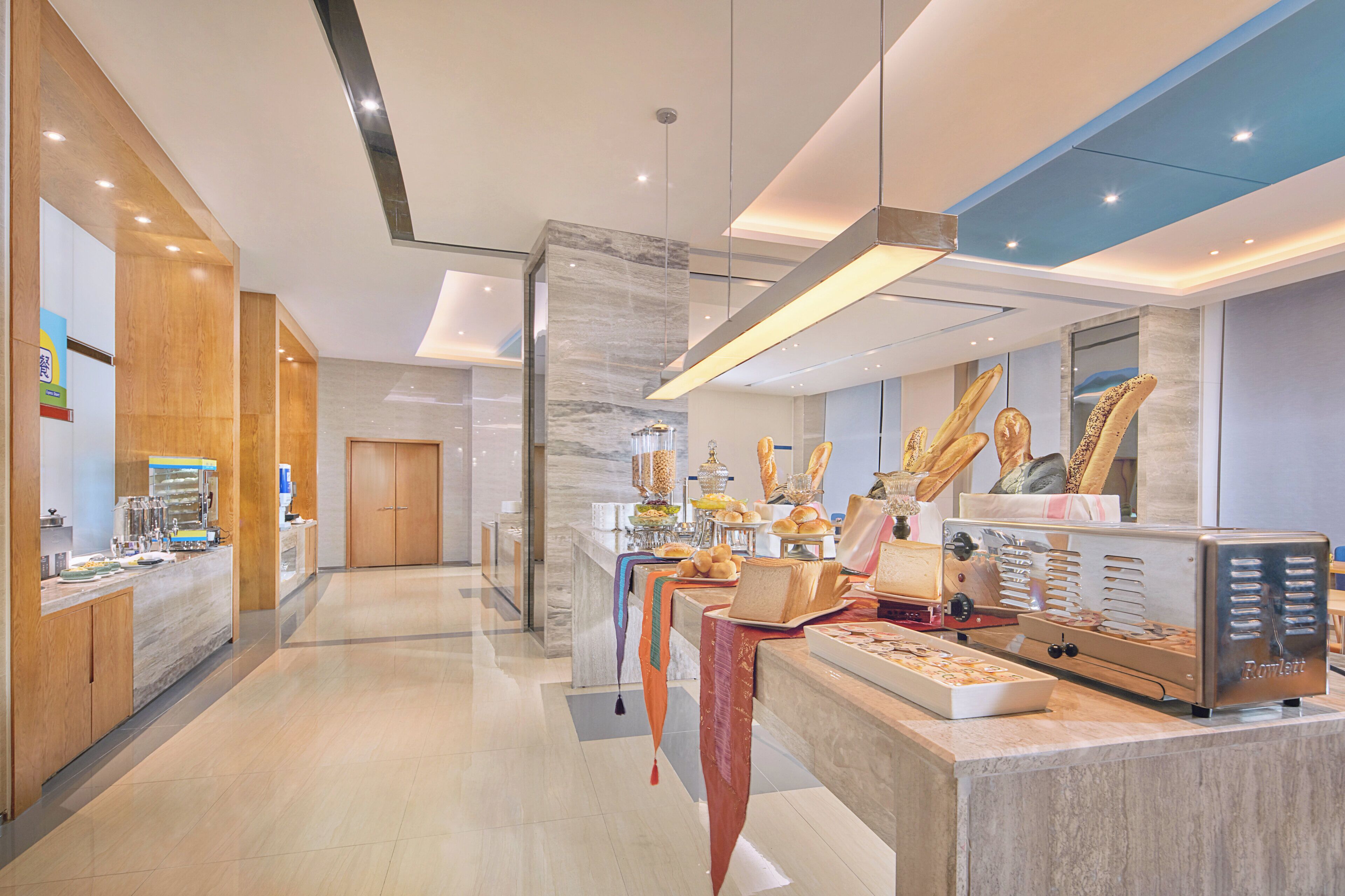 A modern hotel lobby with a reception desk, a seating area with a buffet, and a large window offering a view of the cityscape.