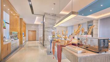 Un hall d’hôtel moderne comprenant un comptoir d’accueil, un espace salon avec un buffet, et une grande fenêtre offrant une vue sur le paysage urbain.