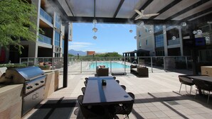 Une terrasse extérieure équipée d’un barbecue, d’une table à manger et de chaises, avec vue sur une piscine et les montagnes.