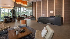 Un hall d’entrée spacieux au design moderne, comprenant un grand espace salon, un comptoir d’accueil et une vue sur l’extérieur grâce à de grandes fenêtres.