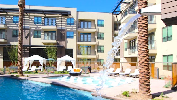 Una piscina con fuente, sillones de descanso y un edificio con balcones.