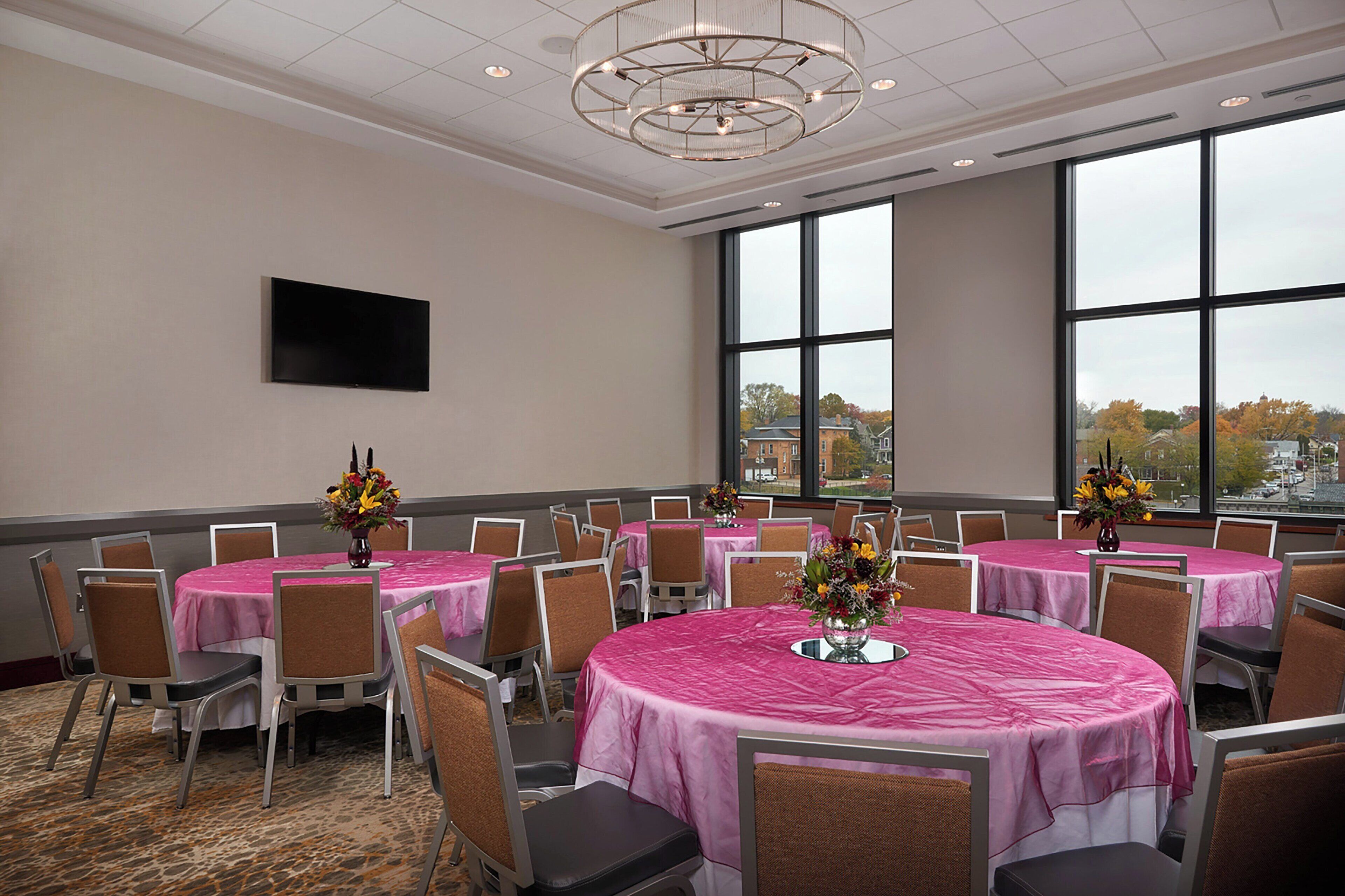 A conference room with multiple tables, chairs, and large windows offering a view of the cityscape.