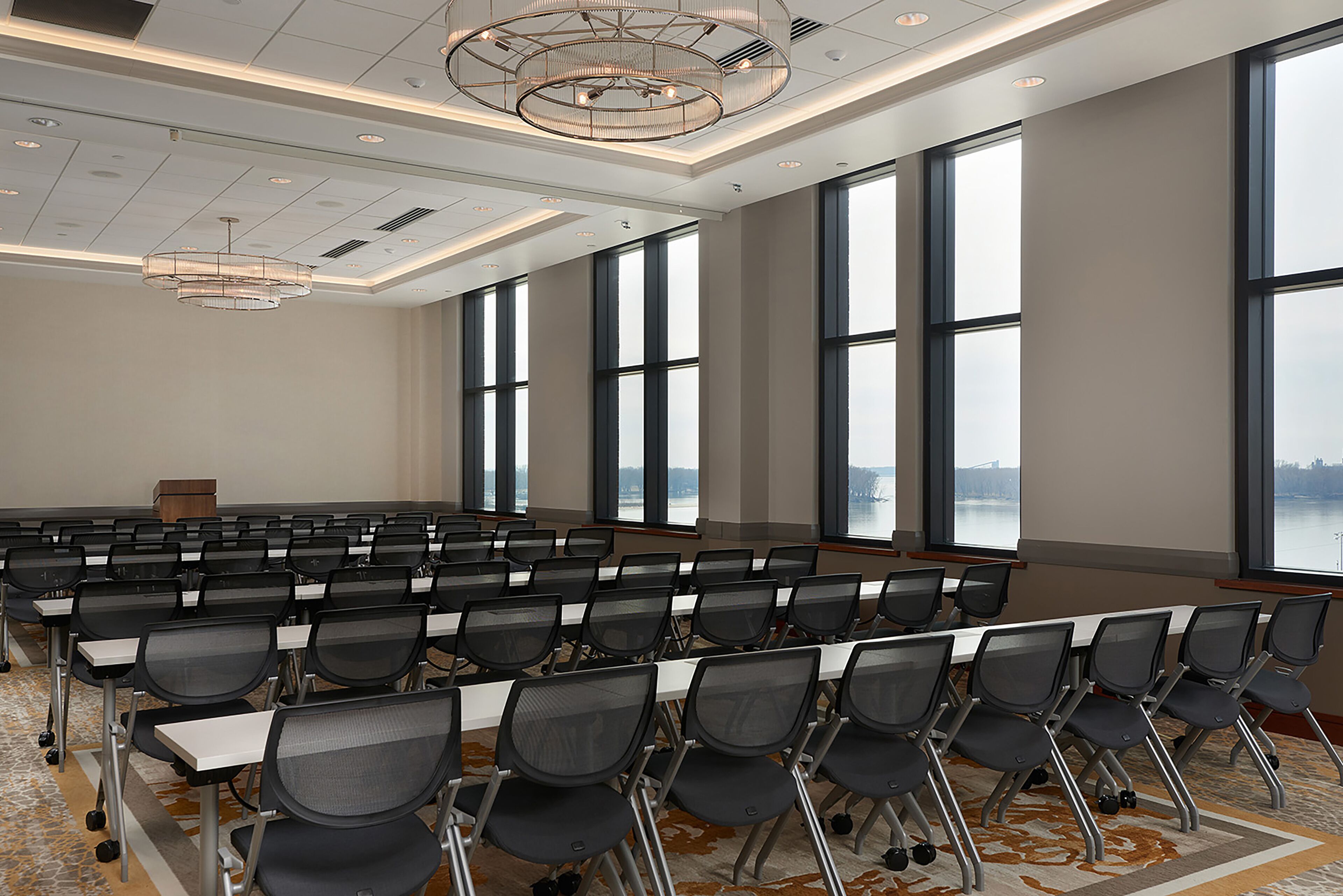 A conference room with rows of chairs, large windows, and a chandelier.