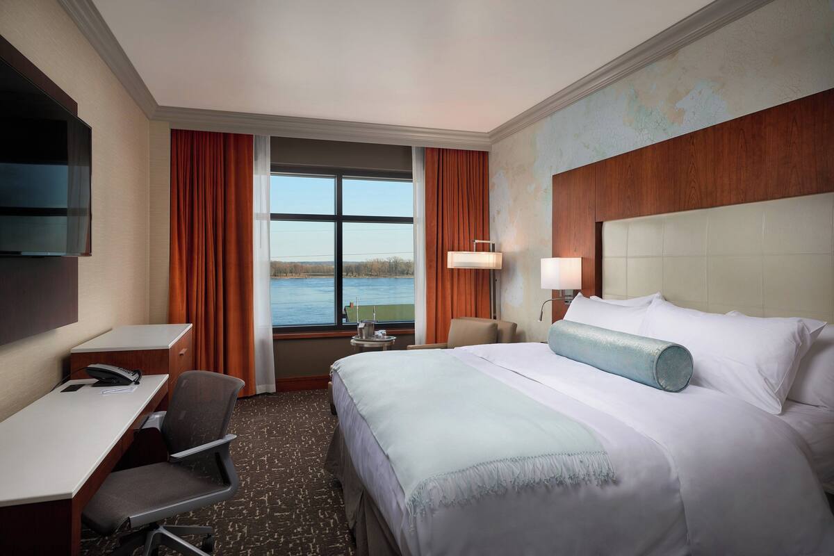 A hotel room with a bed, desk, chair, and a view of the water.