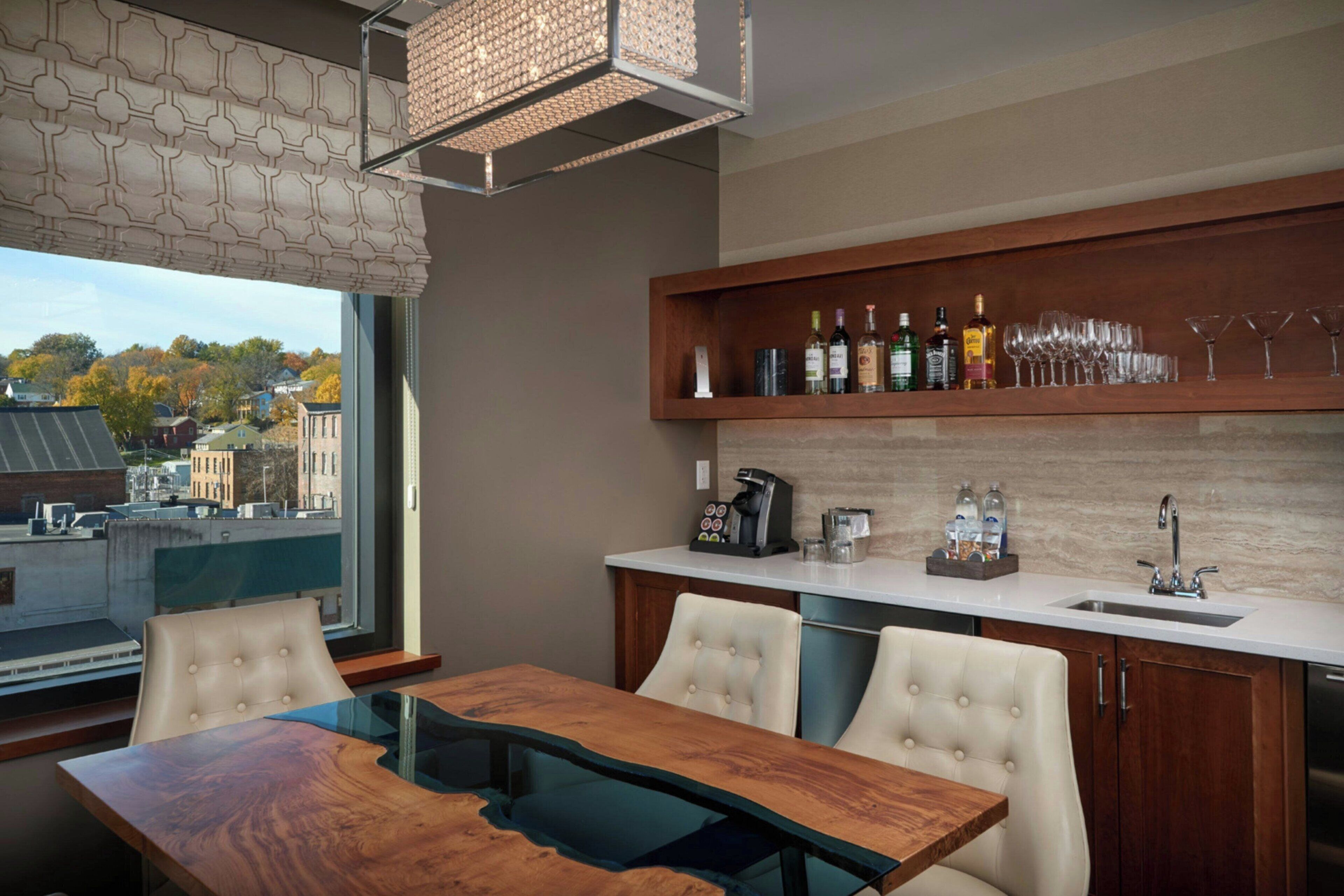 A modern kitchen with a dining area, featuring a wooden table, chairs, a coffee machine, and a wine and liquor shelf.