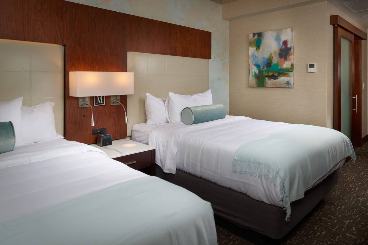 A hotel room with two beds, a wooden headboard, a nightstand with a lamp, and a painting on the wall.