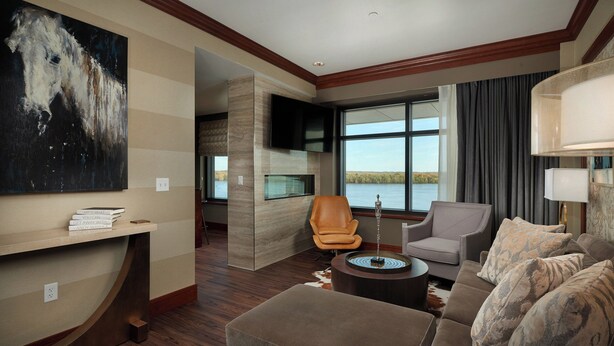 Un salon moderne avec un grand tableau, un canapé, deux fauteuils, une table basse et une vue sur un lac, visible à travers de grandes fenêtres.