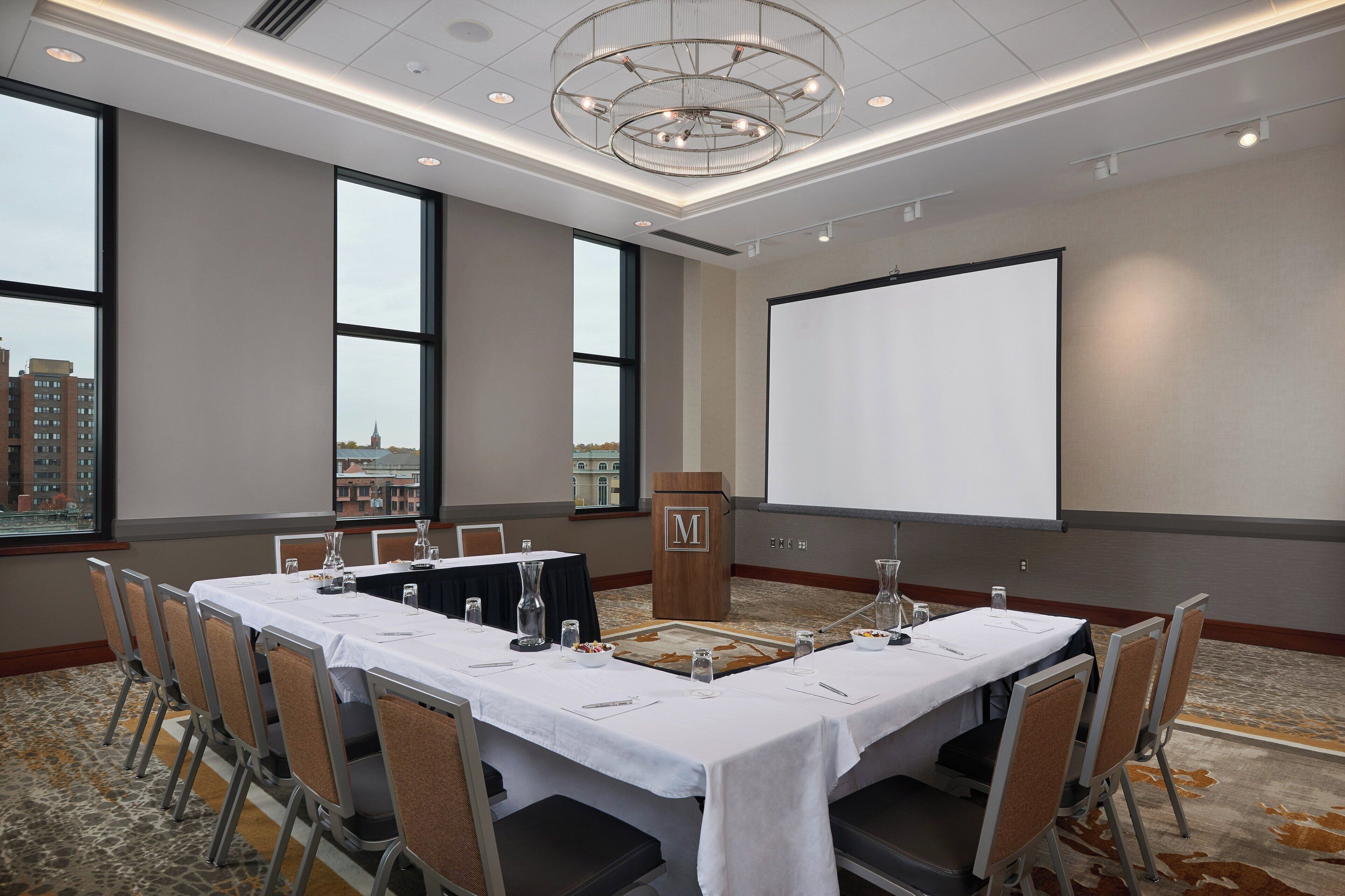 A conference room with a long table, chairs, a podium, and a projector screen.