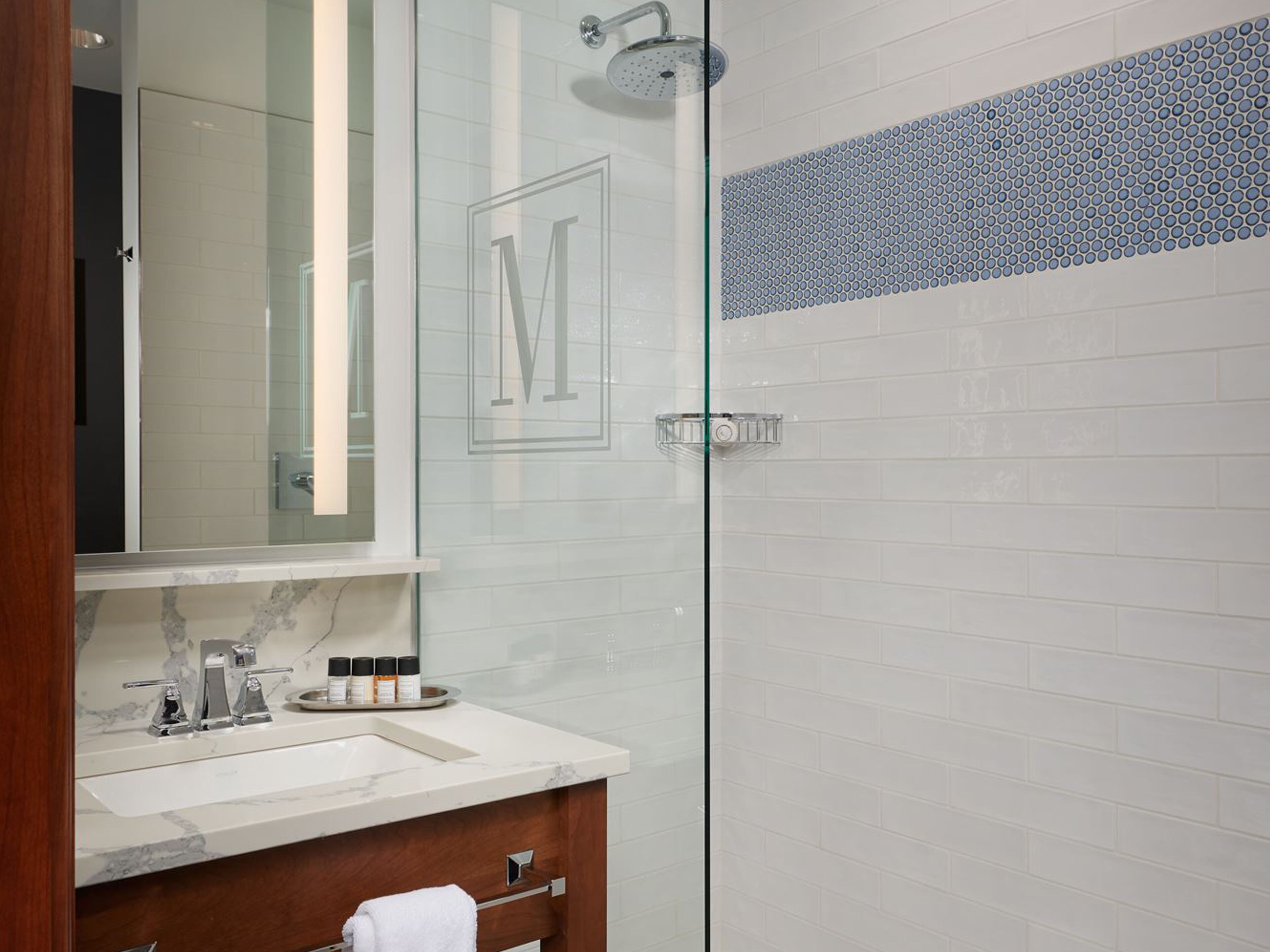A modern bathroom with a glass shower enclosure, a marble sink, and a vanity with a mirror.