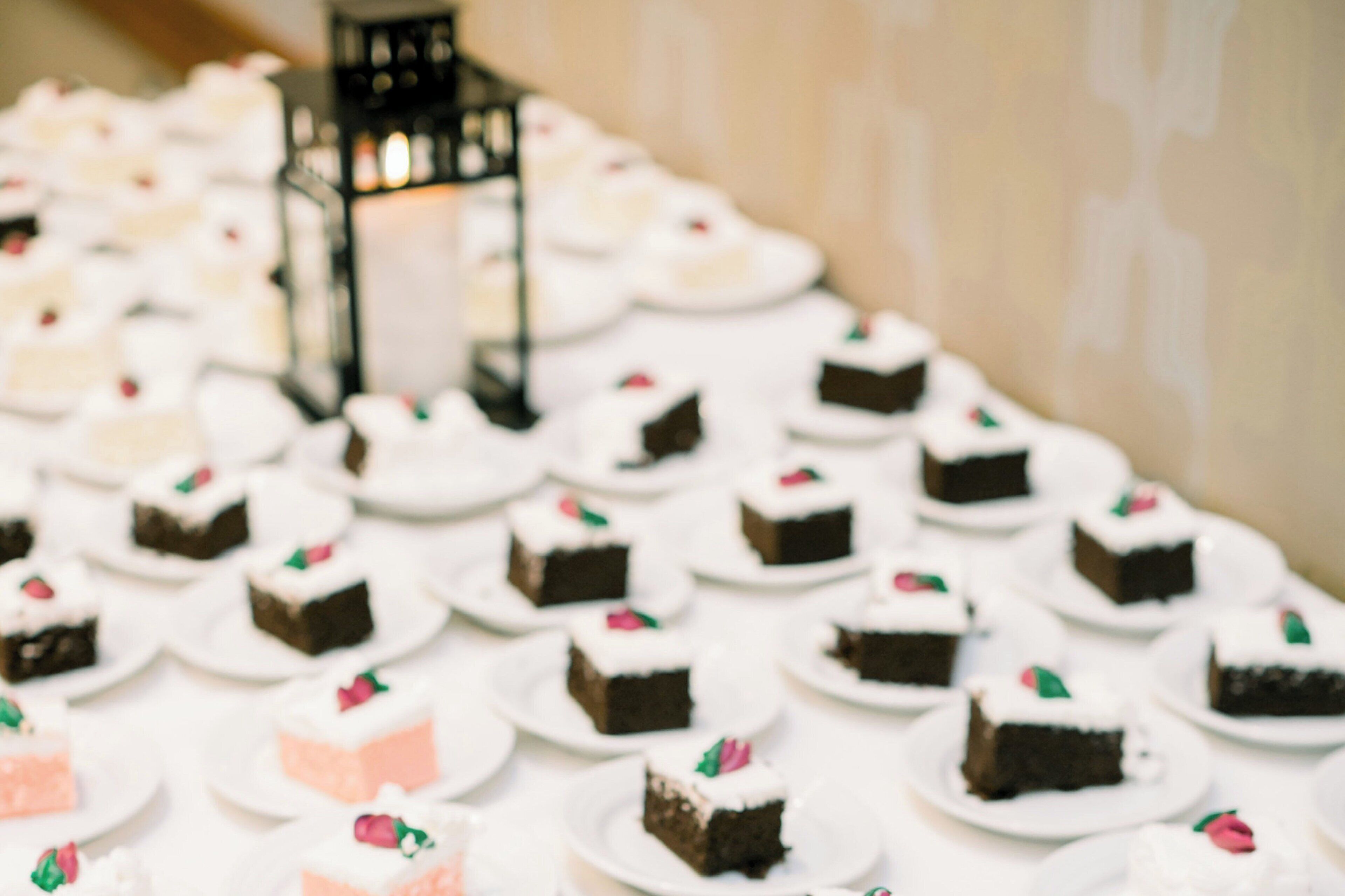 A table with multiple plates of cake, some with white frosting and others with pink frosting, arranged in rows.