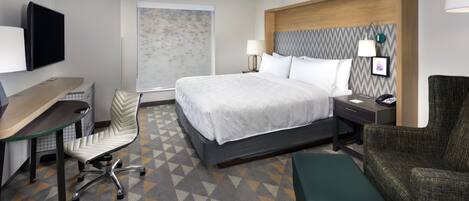 A hotel room with a bed, desk, chair, and a TV.
