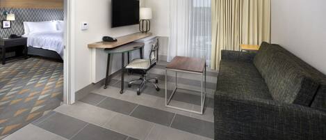 A hotel room with a bed, a desk with a chair, a sofa, and a TV.