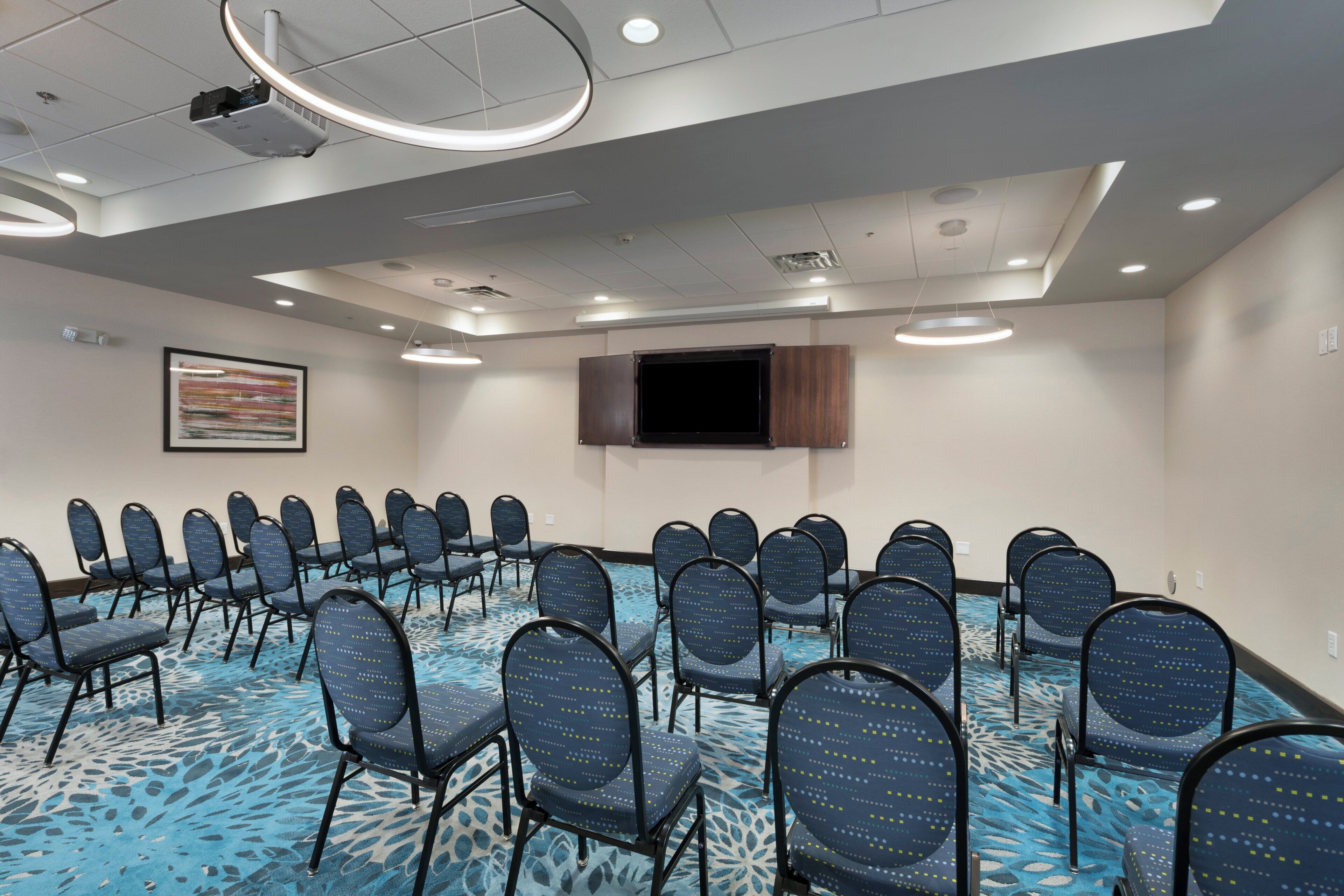 Un salón de conferencias con filas de sillas, una televisión instalada y una alfombra estampada.