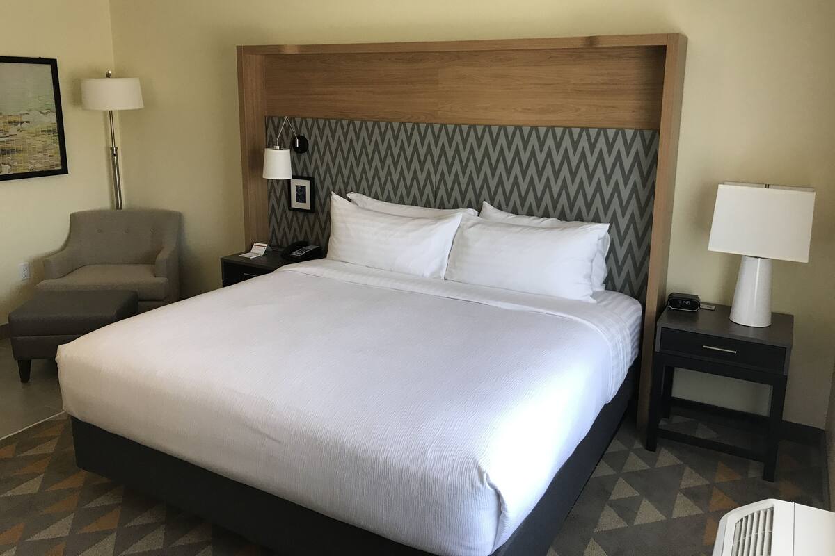 Une chambre d’hôtel avec un grand lit, une chaise, une table de chevet avec une lampe et une horloge murale.