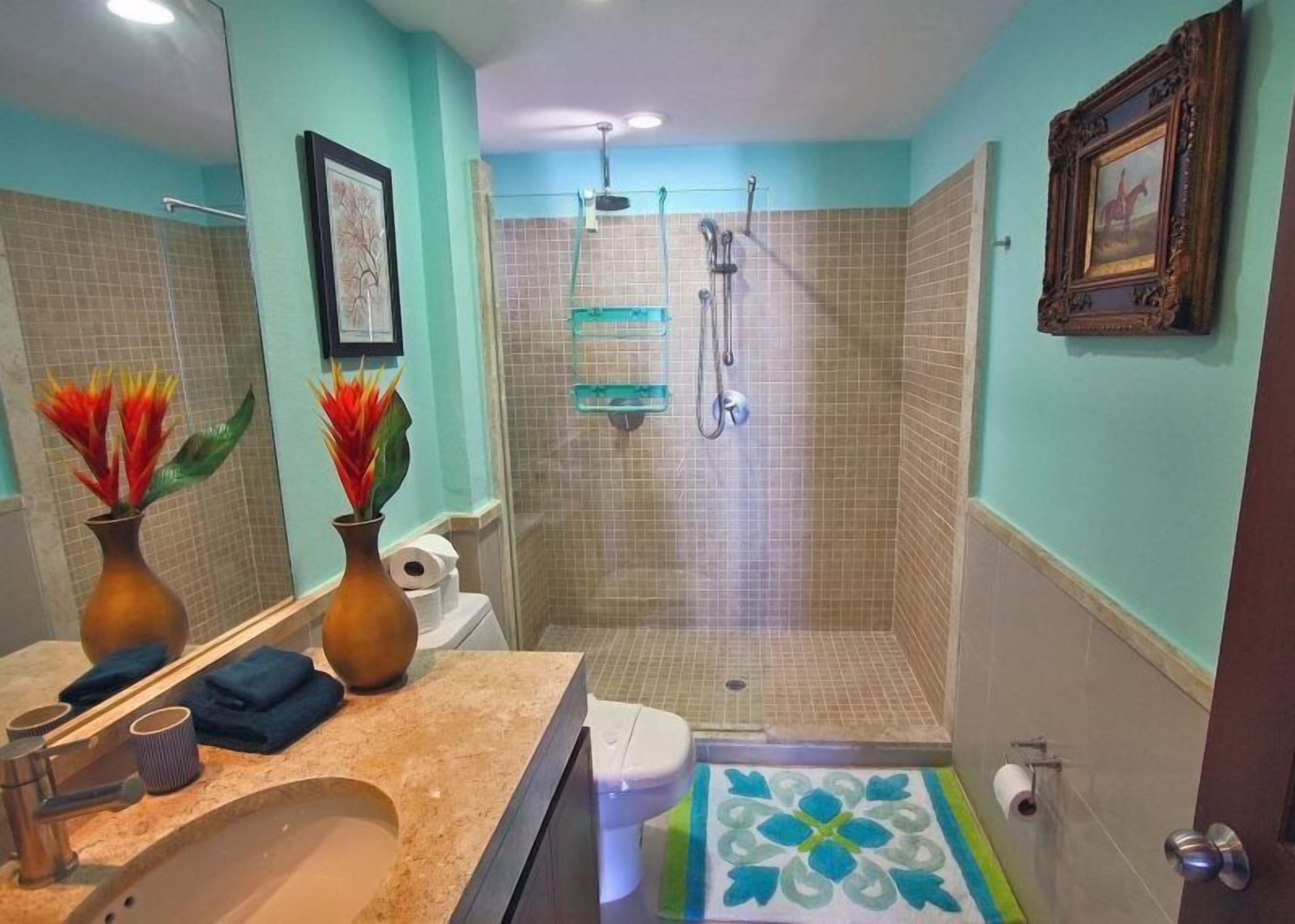 A bathroom with a shower, a sink, and a toilet. There are two vases with flowers on the counter.