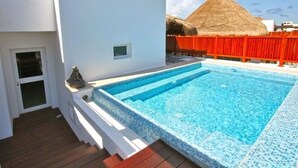 A swimming pool with a white deck and a thatched-roof structure in the background. - Kaan 302 by NAS (Playa del Carmen)