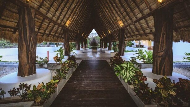 A covered walkway with a thatched roof, flanked by planters with tropical plants, leading to a central area with a view of the beach. - Kaan 302 by NAS (Playa del Carmen)