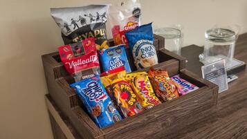 A wooden box filled with various snack packages including Valetta, Club Social, Inka Corn, and others.