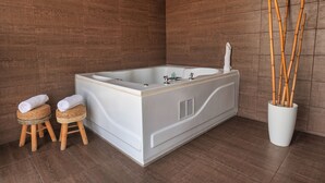 A modern bathroom with a large bathtub, two wooden stools with towels, and a bamboo plant in a white pot.