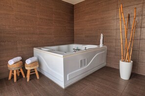 A modern bathroom with a large bathtub, two wooden stools with towels, and a bamboo plant in a white pot. - Rado Hotel - Santa Maria (Trujillo)