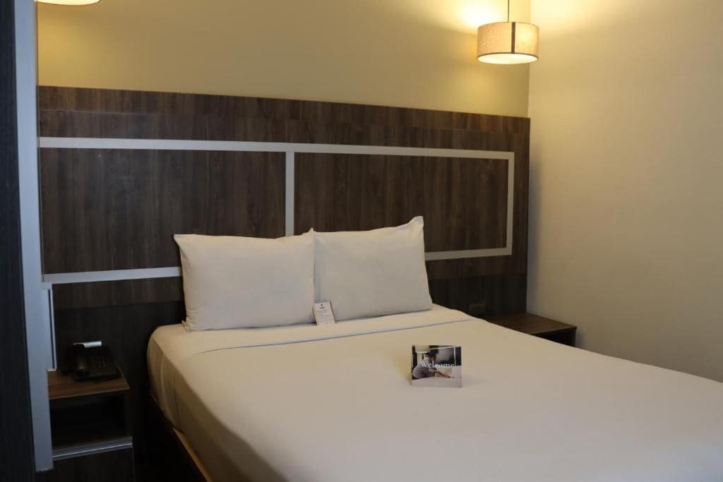 A hotel room with a large bed, a bedside table, and a wall-mounted lamp.