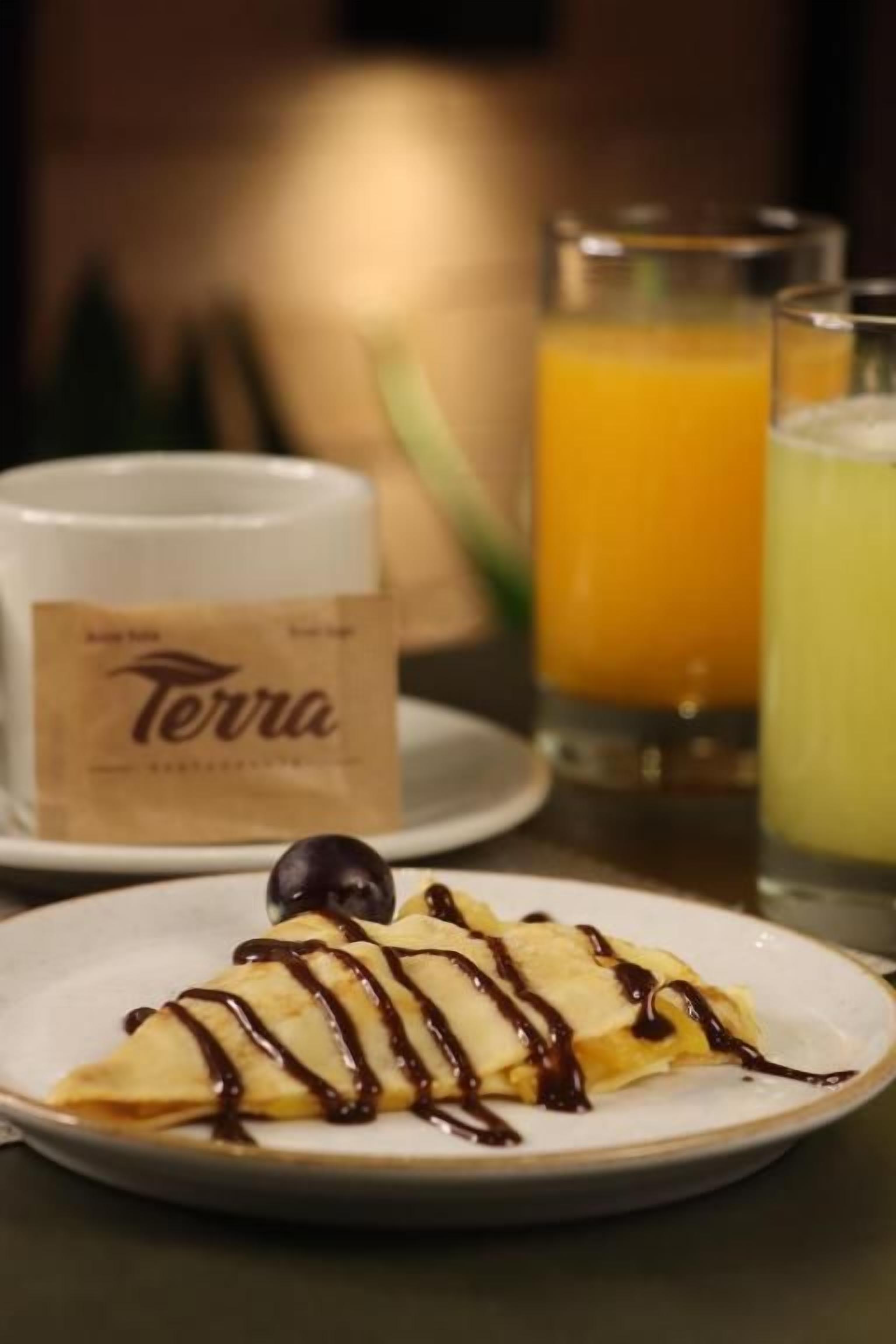 Une assiette avec un dessert, un verre de jus d’orange et un verre d’une boisson jaune sur une table.
