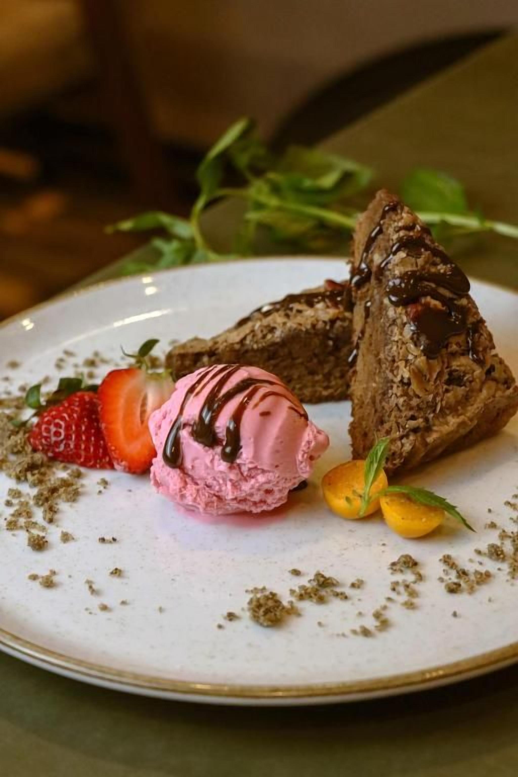 A plate with a dessert consisting of a chocolate-covered pastry, a strawberry, and a scoop of pink ice cream.