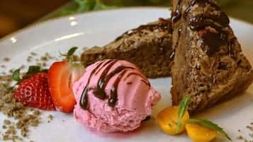 A plate with a dessert consisting of a chocolate-covered pastry, a strawberry, and a scoop of pink ice cream.