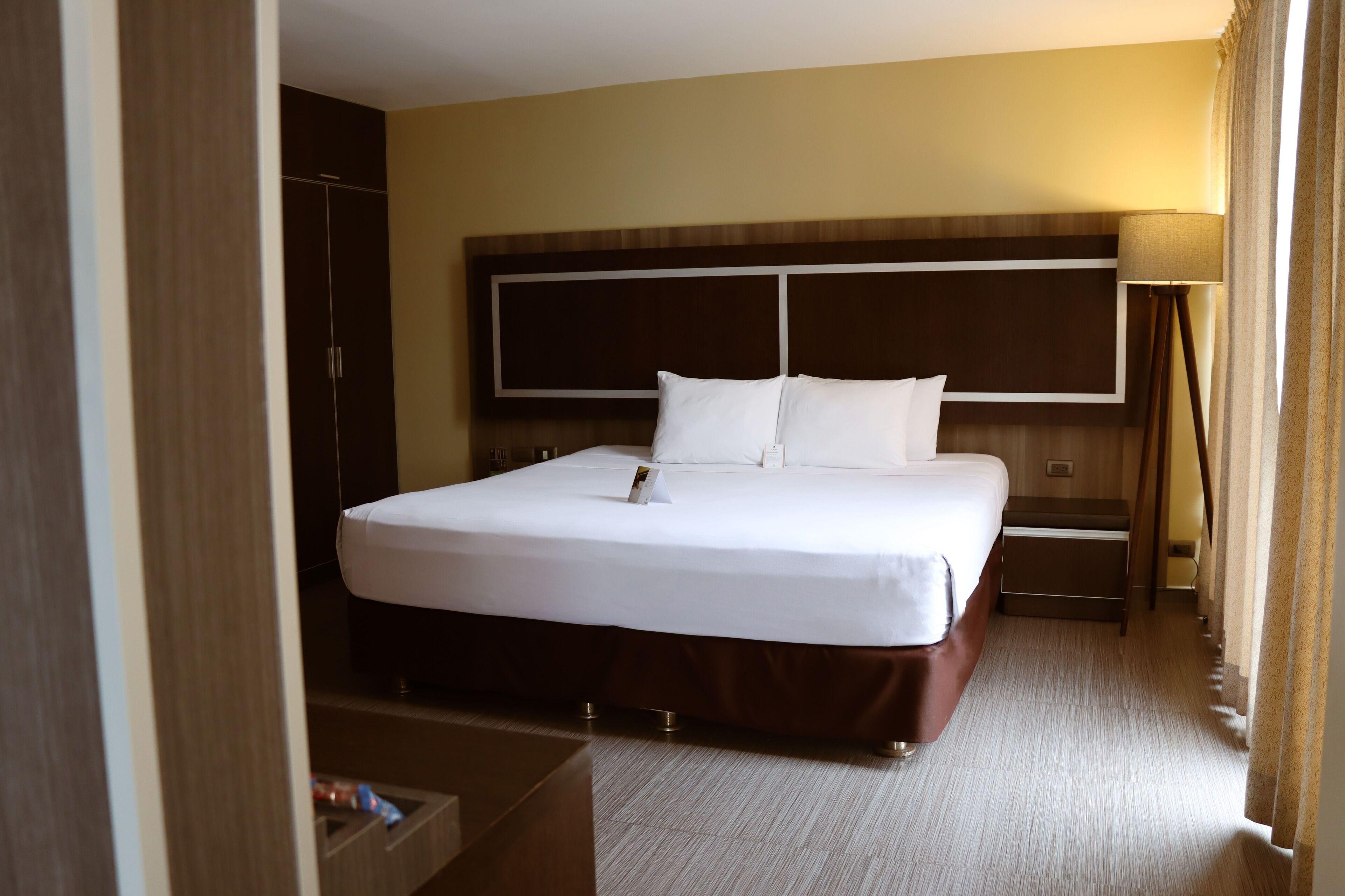 Habitación de hotel con una cama grande, un armario, una mesita de noche y una lámpara.