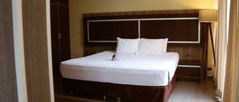 Habitación de hotel con una cama grande, un armario, una mesita de noche y una lámpara.