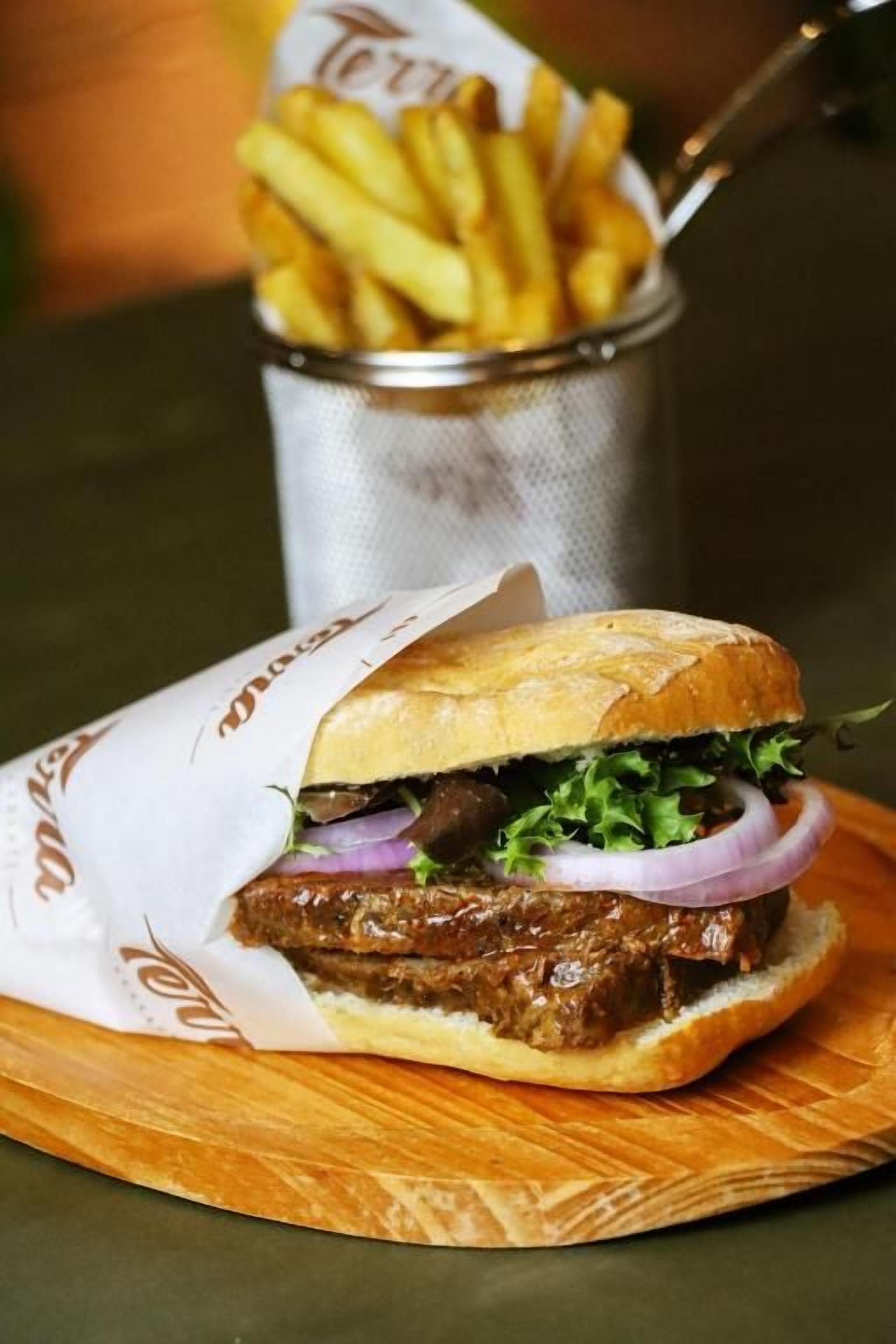 A sandwich with lettuce, red onion, and a side of fries on a wooden board.