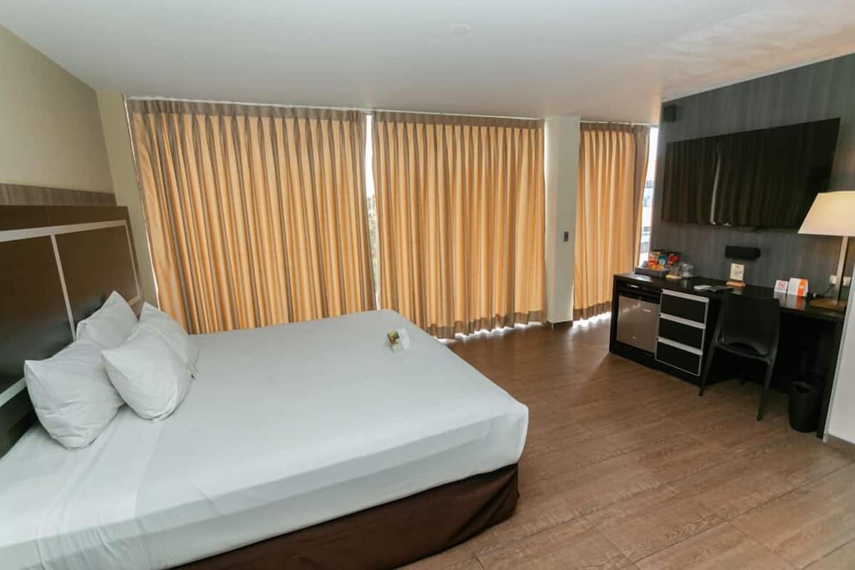 A hotel room with a large bed, a desk with a chair, a TV, and curtains.