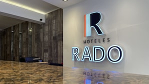 En hotellobby med en marmorskiva i receptionen, en väggpanel i trä och upplysta skyltar med texten ”HOTELES RADO”.