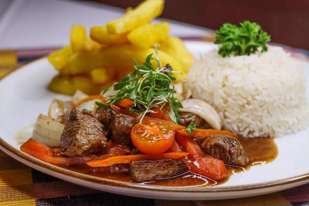 A plate with a beef stew, rice, and fried plantains.