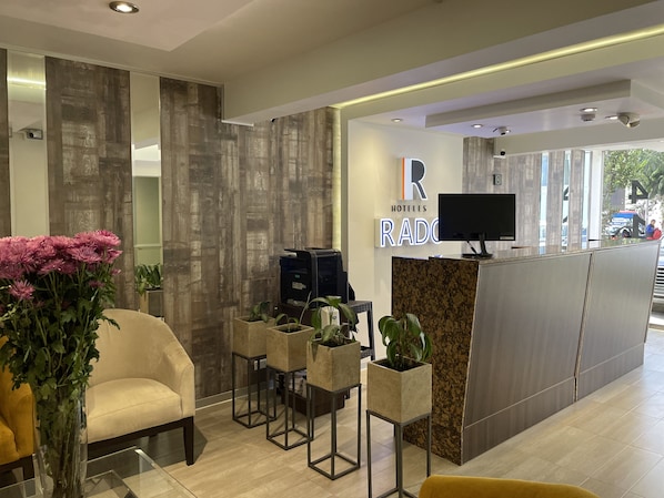 A hotel reception area with a modern design, featuring a reception desk, seating area, and potted plants. - Rado Hotel - Santa Maria (Trujillo)