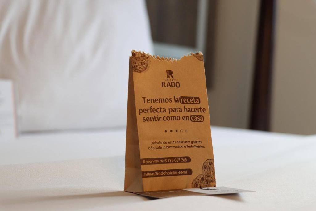 A brown paper bag with text, placed on a white surface, likely a hotel room.