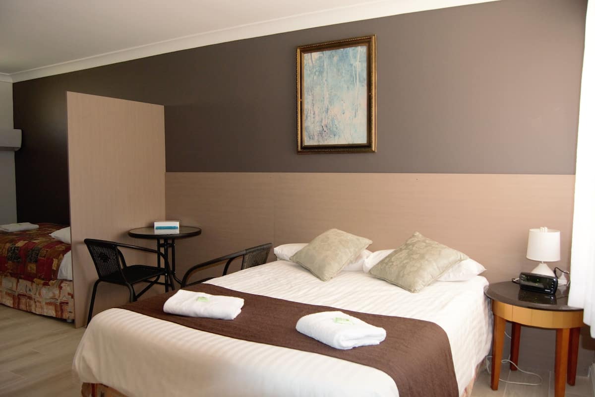 A hotel room with a bed, two chairs, a small table, a lamp, and a painting on the wall.