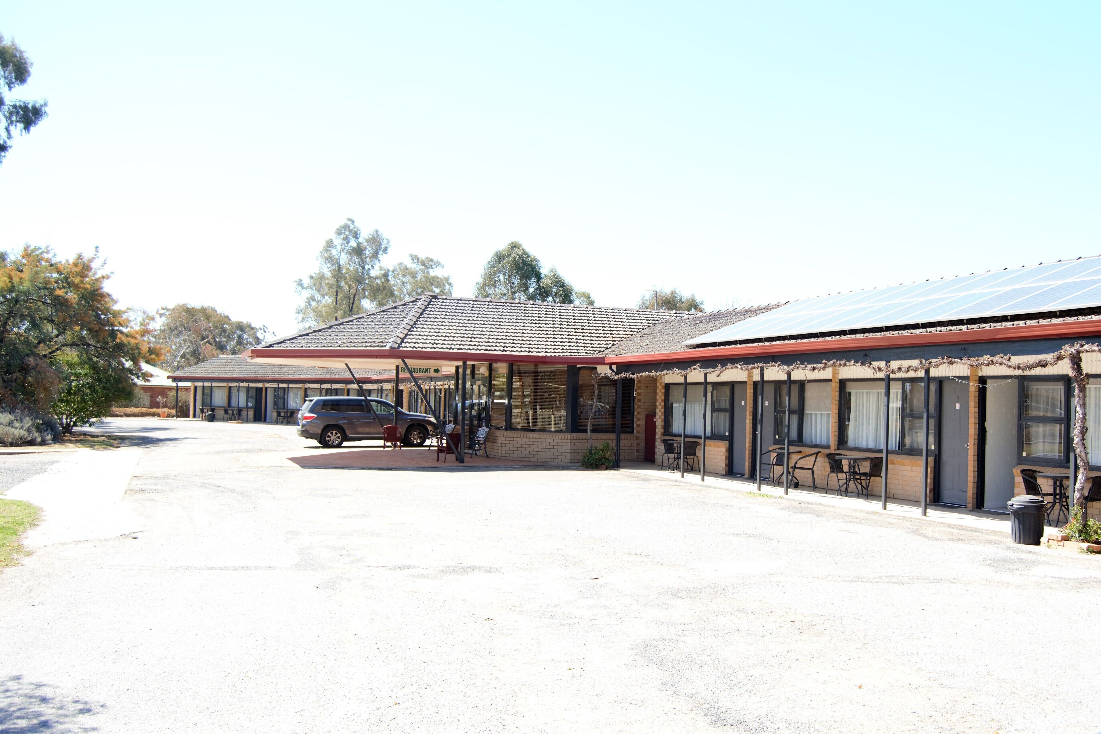 A building with a covered parking area, outdoor seating, and a solar panel array.