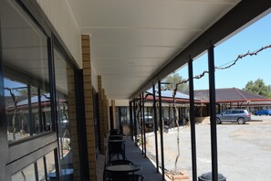 A covered outdoor seating area with tables and chairs, a brick wall, and a view of a parking lot with cars.