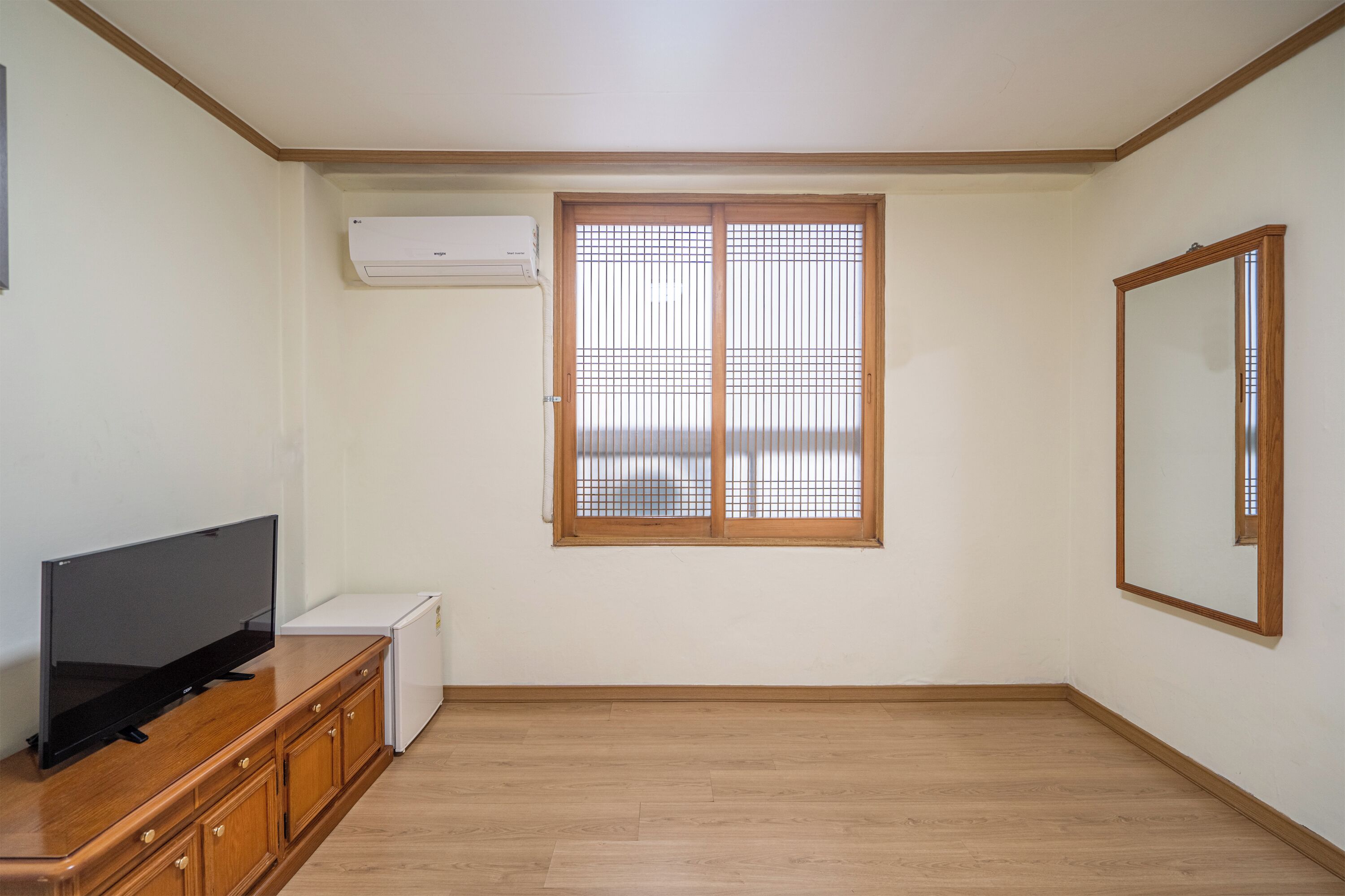 A room with a wooden cabinet, a television, a small white appliance, and a window with wooden blinds.