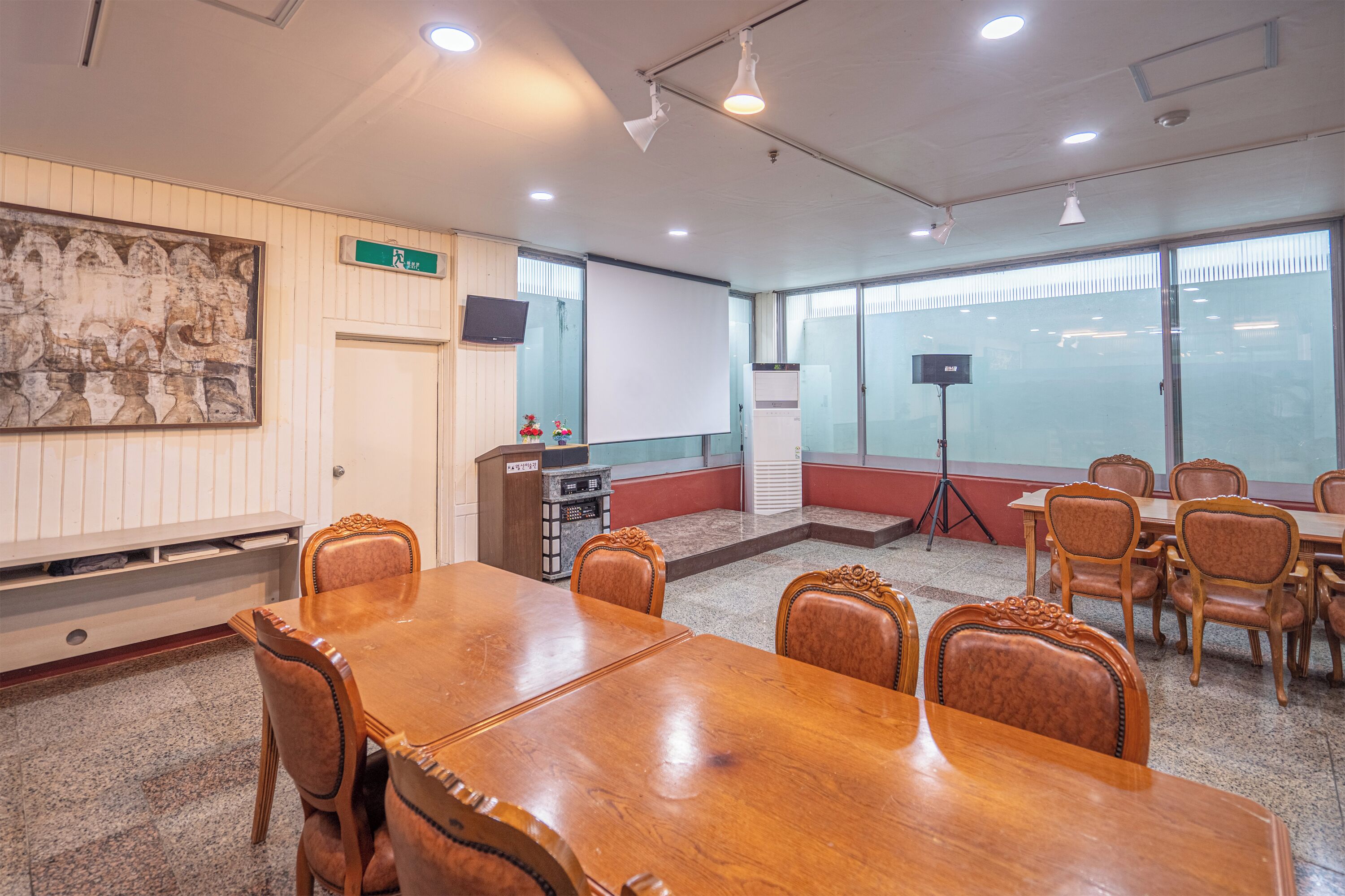 Un salón de conferencias con una mesa y sillas de madera, una pizarra, un proyector y un amplio ventanal con persianas.