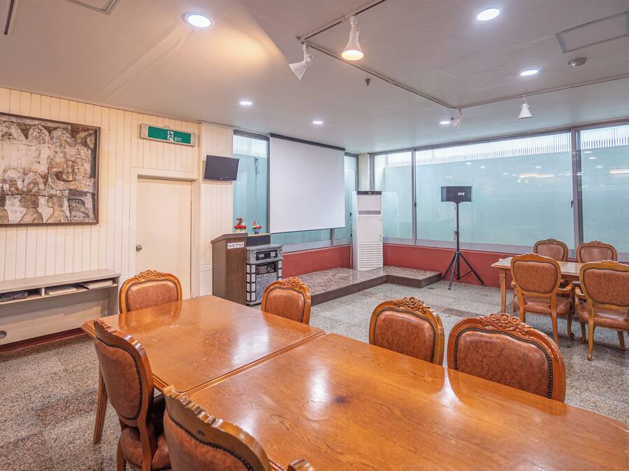 Un salón de conferencias con una mesa y sillas de madera, una pizarra, un proyector y un amplio ventanal con persianas.