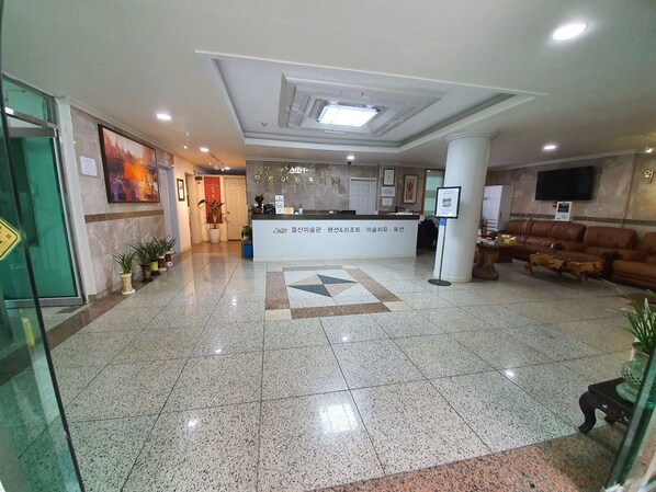 A hotel lobby with a reception desk, a seating area with sofas, and a tiled floor.