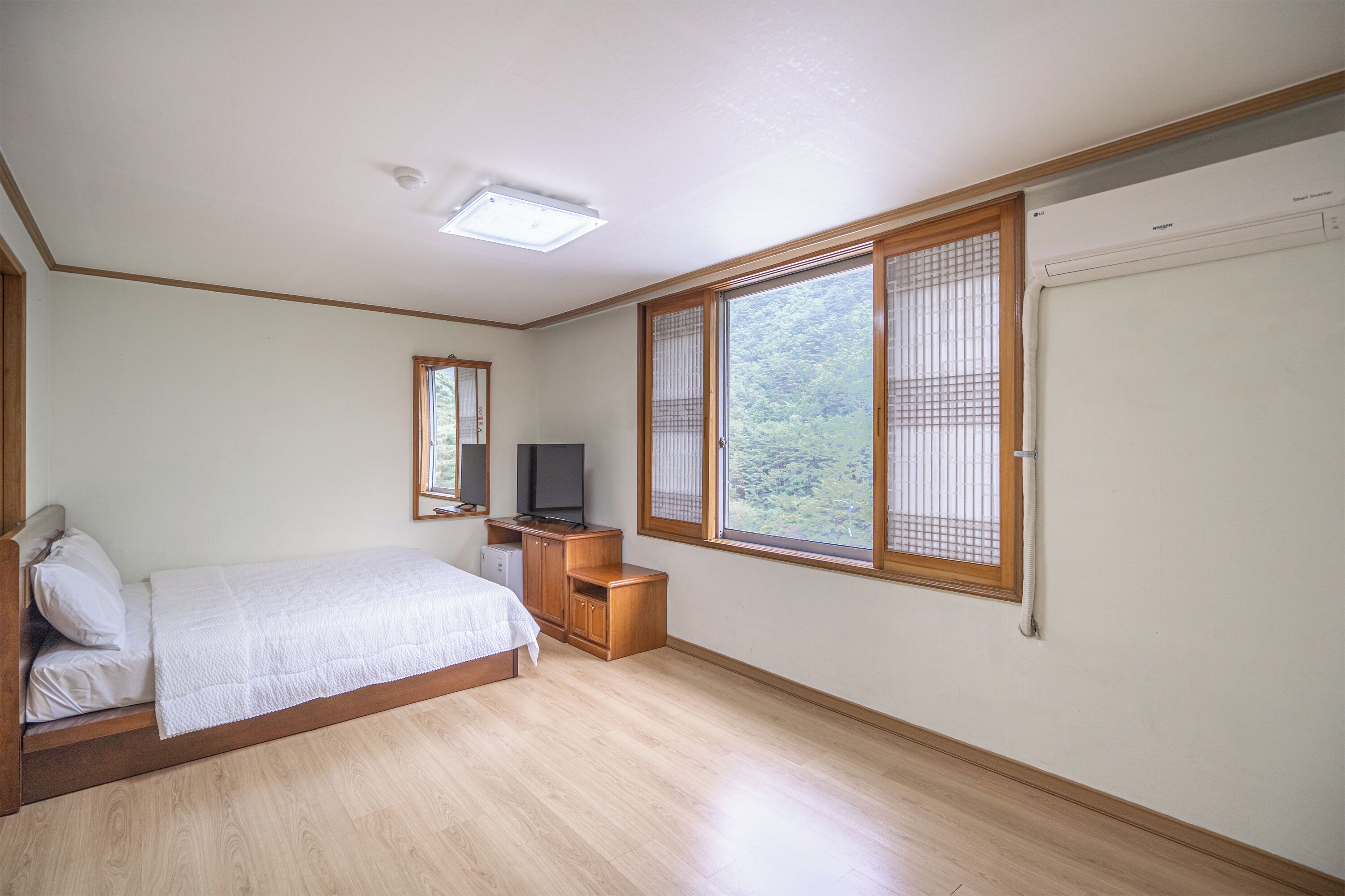 Une chambre à coucher avec un lit, une télévision, une petite table en bois et une fenêtre donnant sur un paysage verdoyant.